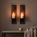 A pair of walnut finish wooden wall candle sconces mounted on a dark wall above a console, both lit with white pillar candles