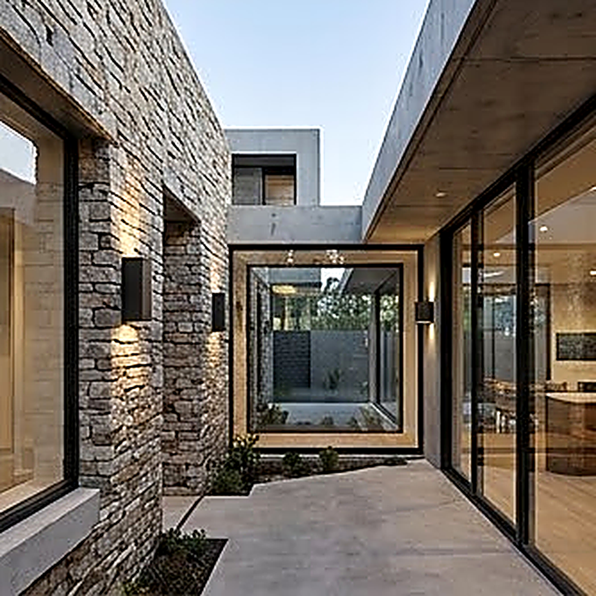 The sconces on a stone courtyard elevation, spaced along the wall beside full height glazing