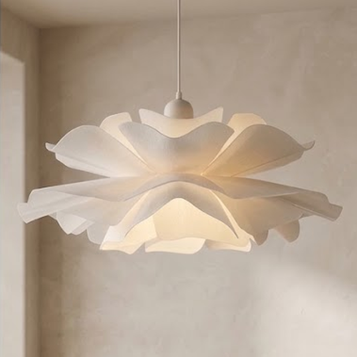 Close view of the lit white petal pendant shade against a plaster wall
