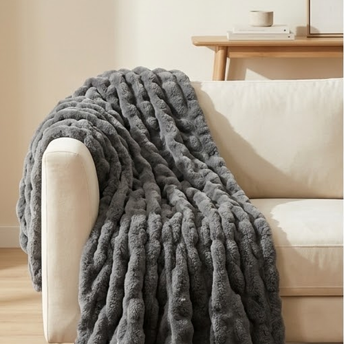 Charcoal grey ruched faux fur throw draped over the arm of a cream sofa onto a jute rug