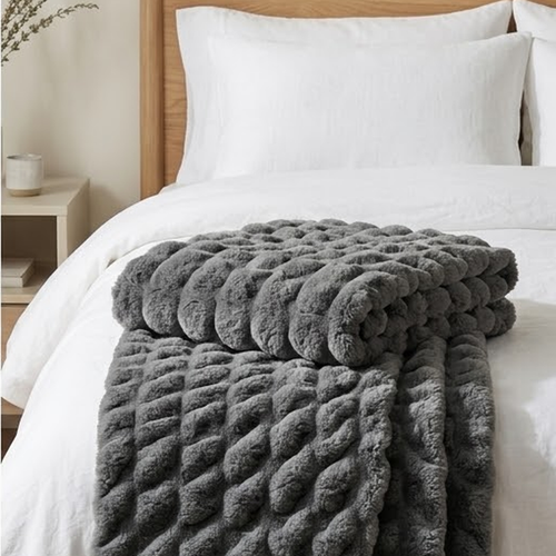 The grey throw folded across the foot of a bed with white linen bedding, showing its thickness