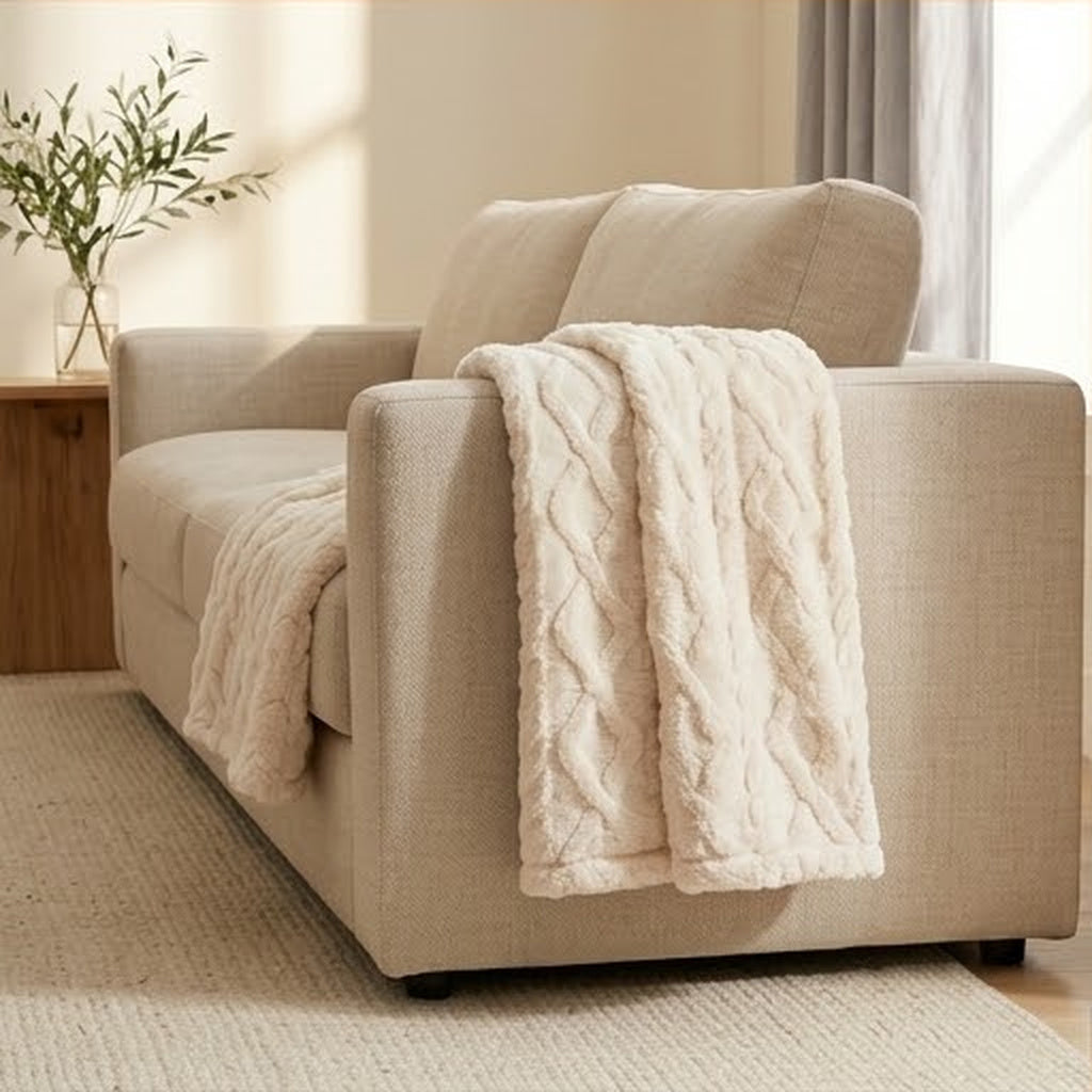 Cream cable faux fur lap throw draped over the arm of a linen sofa