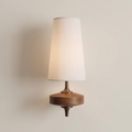 White fabric cone wall sconce on a turned walnut base against a pale wall