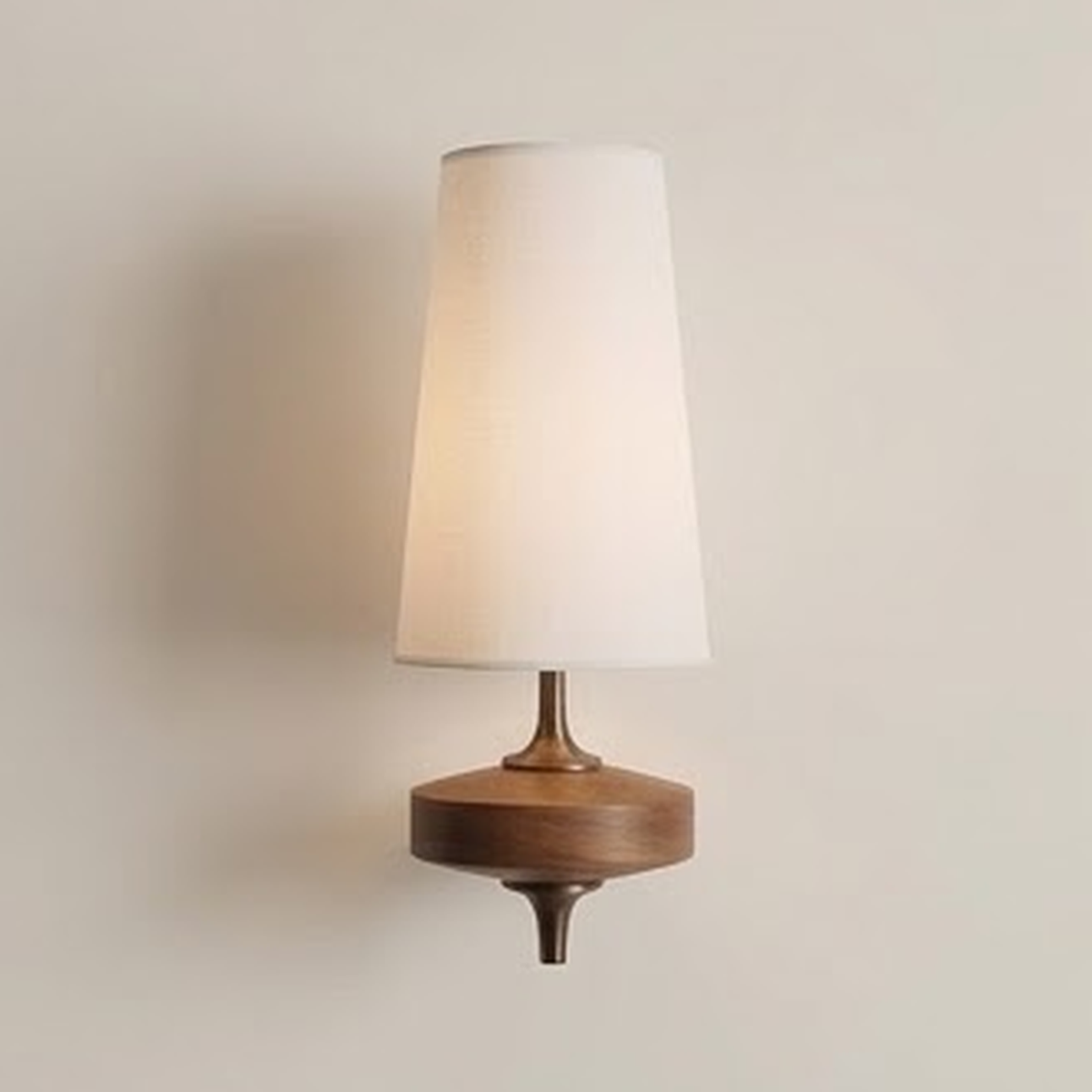 White fabric cone wall sconce on a turned walnut base against a pale wall