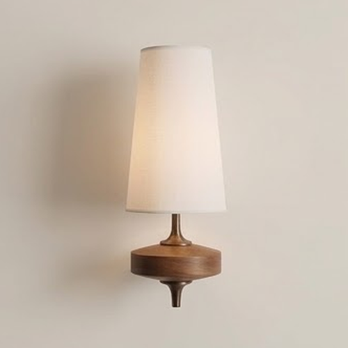White fabric cone wall sconce on a turned walnut base against a pale wall