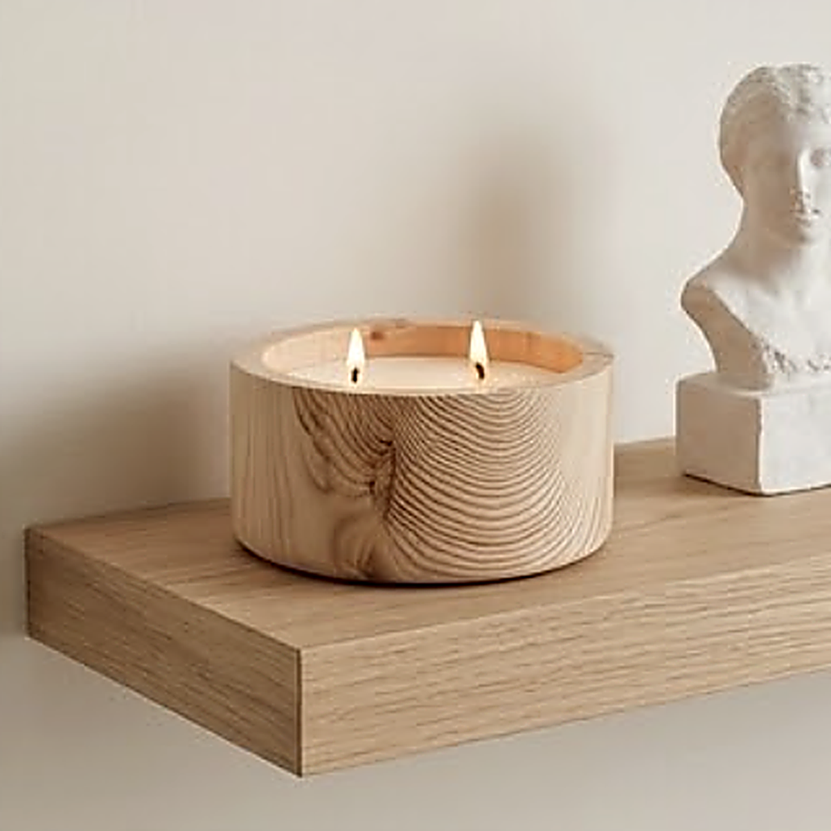 The pale ash finish on an oak floating shelf next to a plaster bust. Wax and wicks not included