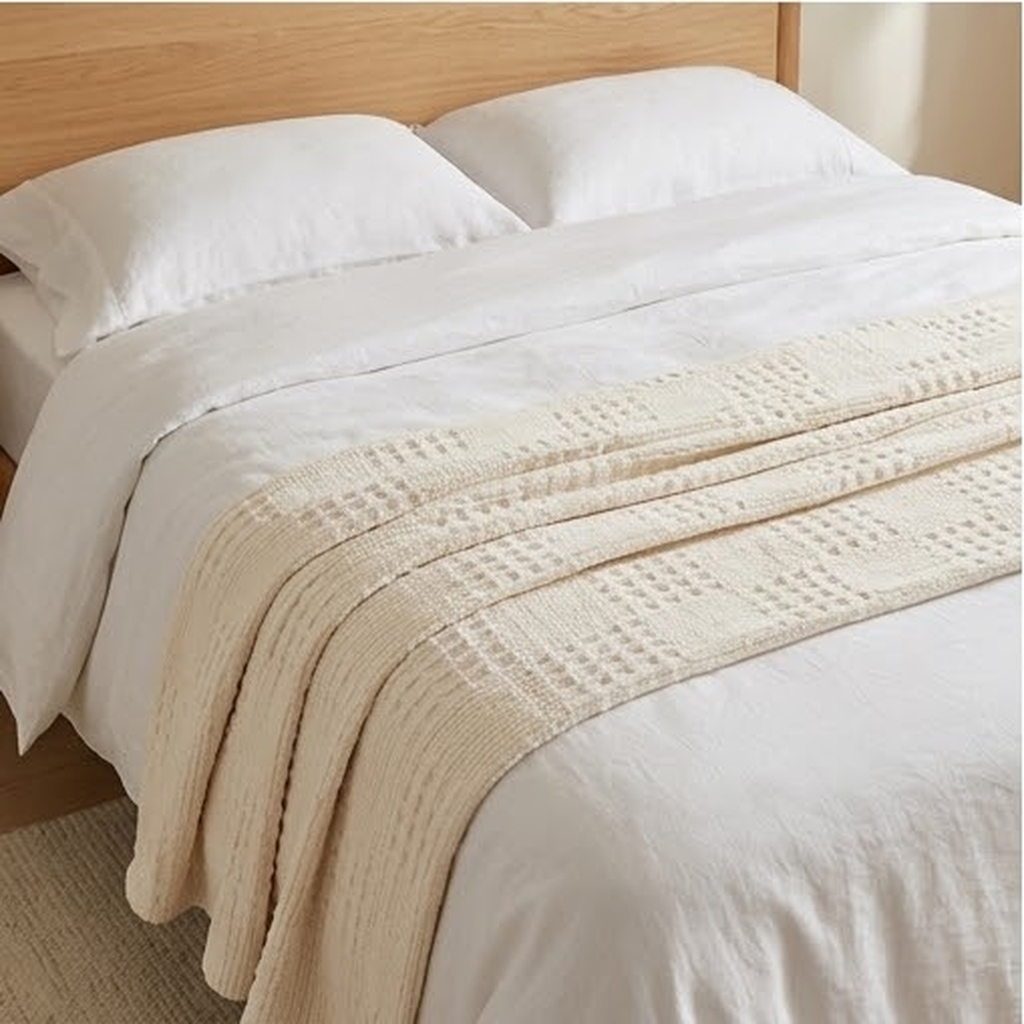 The throw folded across the foot of a bed with white linen bedding
