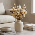 Off white ceramic vase holding dried flowers on a stone coffee table beside stacked books