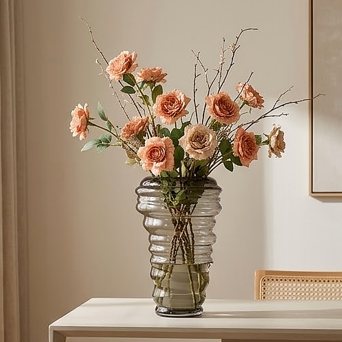 Smoked grey threaded glass vase holding a full bunch of peach roses and branches on a pale console table