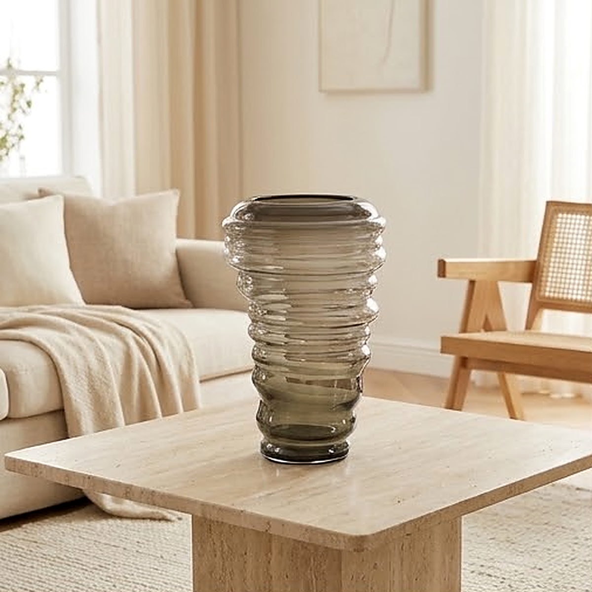 The grey threaded glass vase standing empty on a travertine coffee table beside a cream sofa