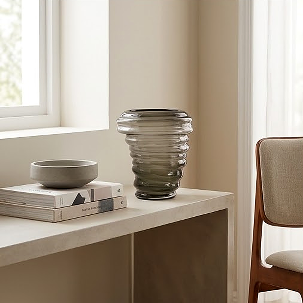 The vase on a console beside a window, its coiled glass bands catching the daylight against stacked books