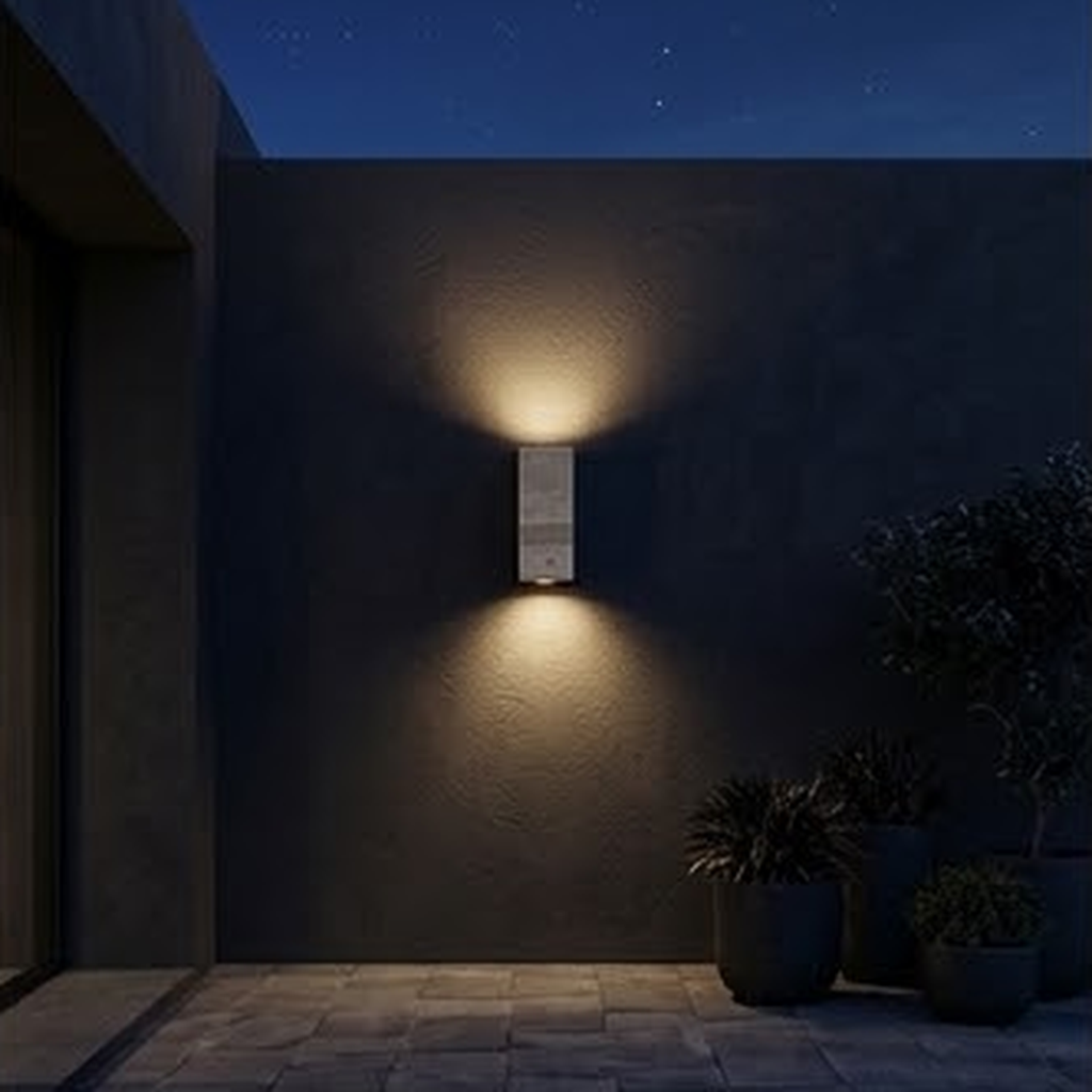 Square travertine sconce lit at night on a dark exterior wall beside potted plants