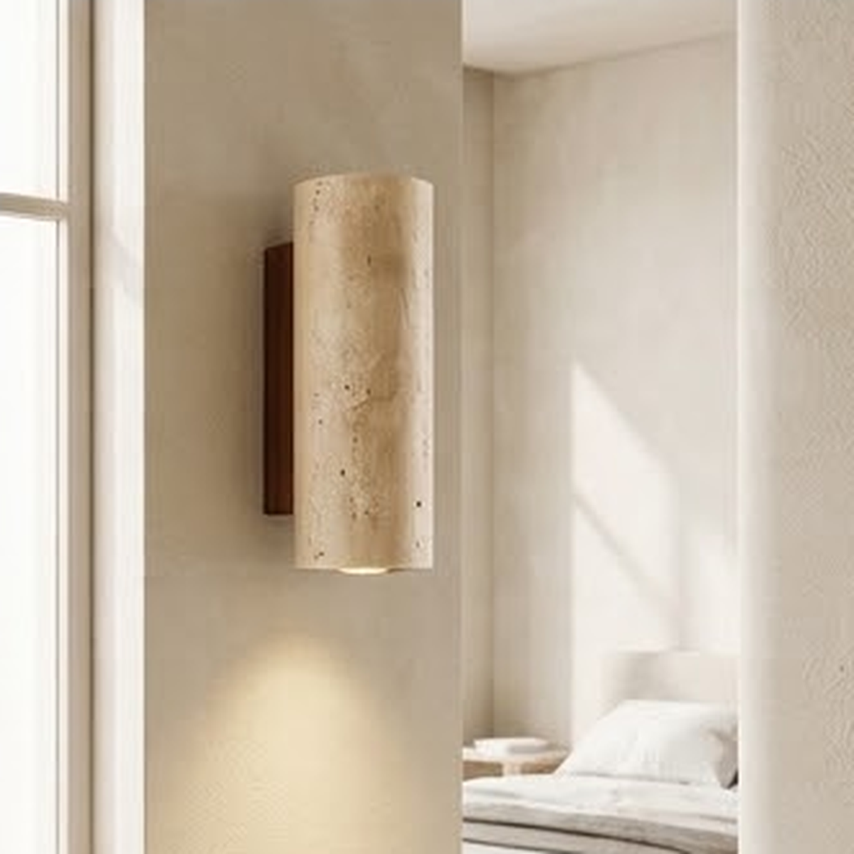 Round travertine wall sconce lit beside a bed in a bright neutral bedroom