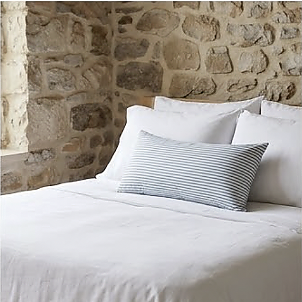 The Stripe pattern as a 30 x 50 cm lumbar cushion across white bed linen against a stone wall. Cover only