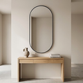 The black framed oval mirror above an oak console table in a bright hallway, showing the thin metal frame