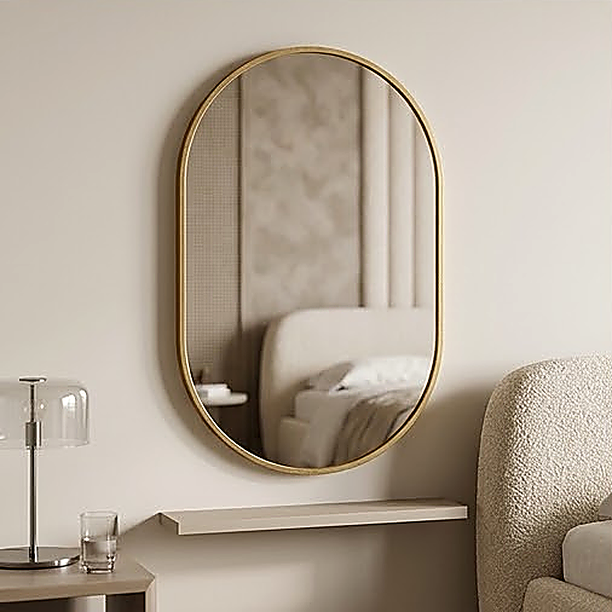 The gold framed oval mirror on a bedroom wall above a floating shelf, reflecting the bed behind