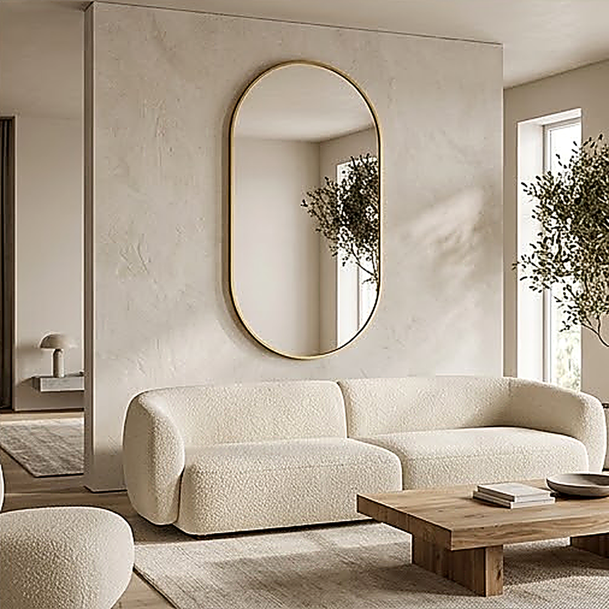 The gold framed oval mirror on a plaster living room wall above a boucle sofa, reflecting an olive tree