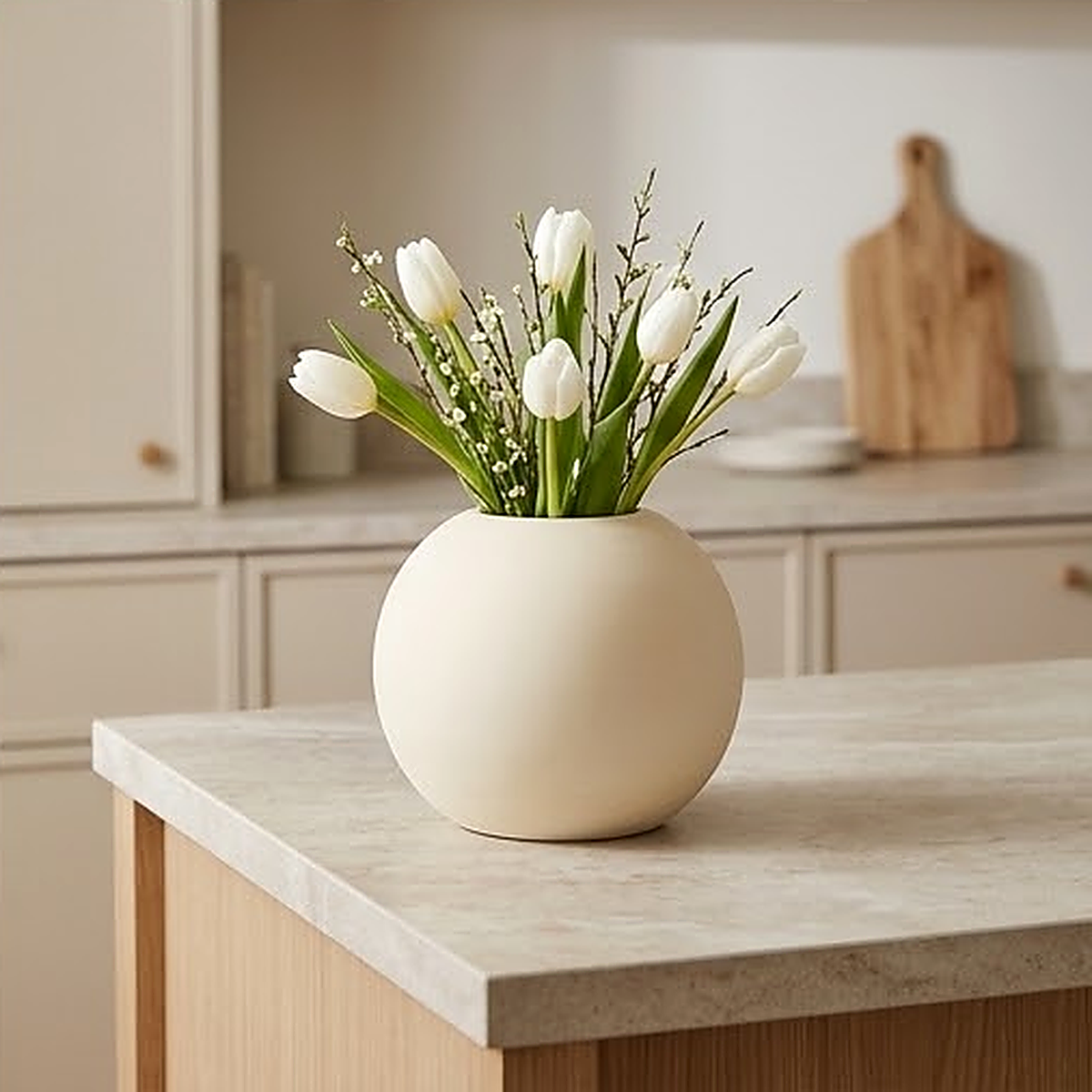 The round sphere vase holding white tulips on a stone topped kitchen island. Use a glass liner for fresh stems