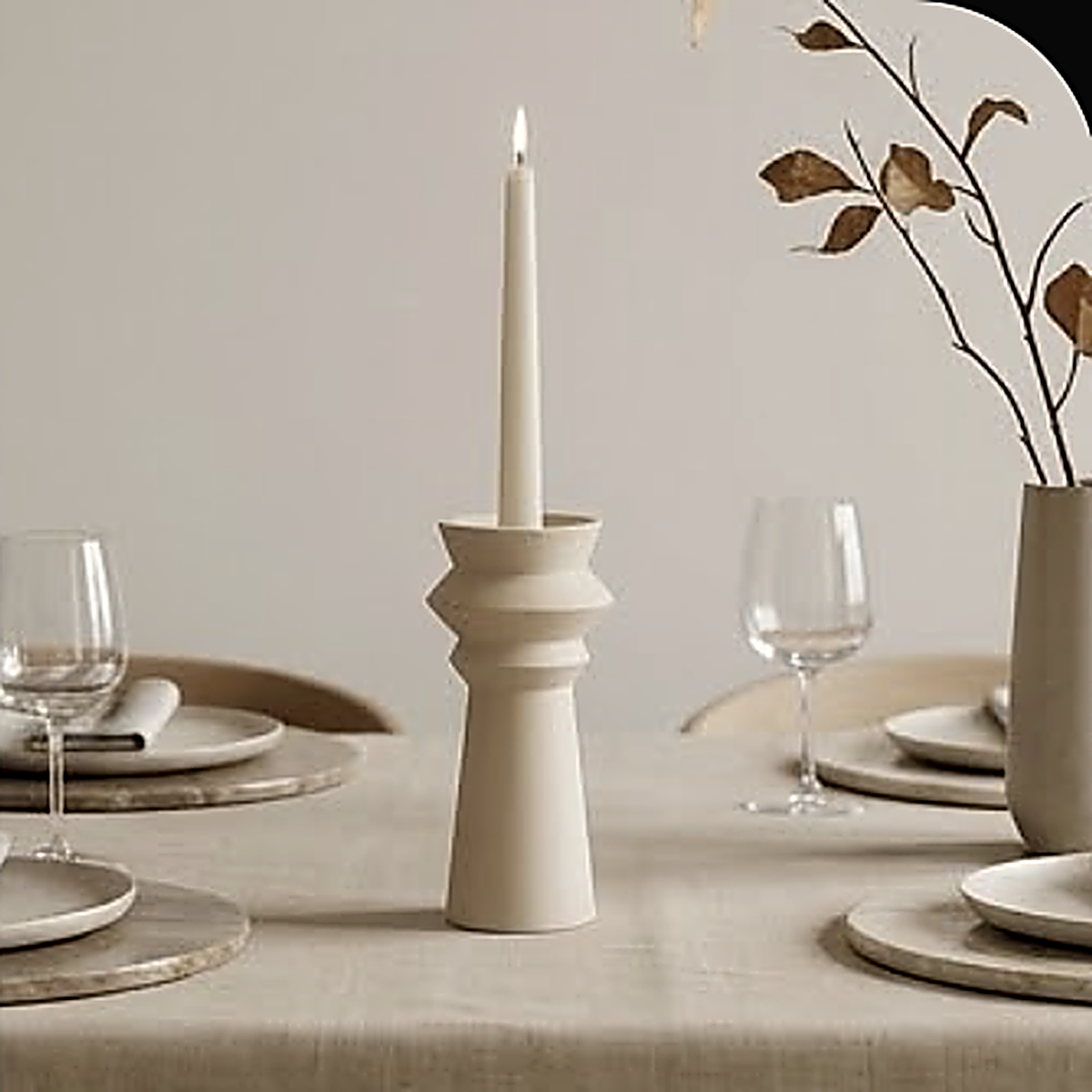 A single stepped ceramic candle holder on a set dining table between wine glasses. Styled with a taper; the maker specifies a tealight