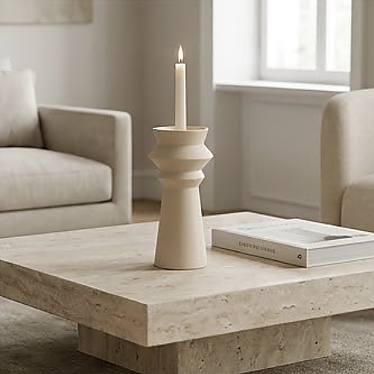 The candle holder lit on a travertine coffee table beside a hardback book