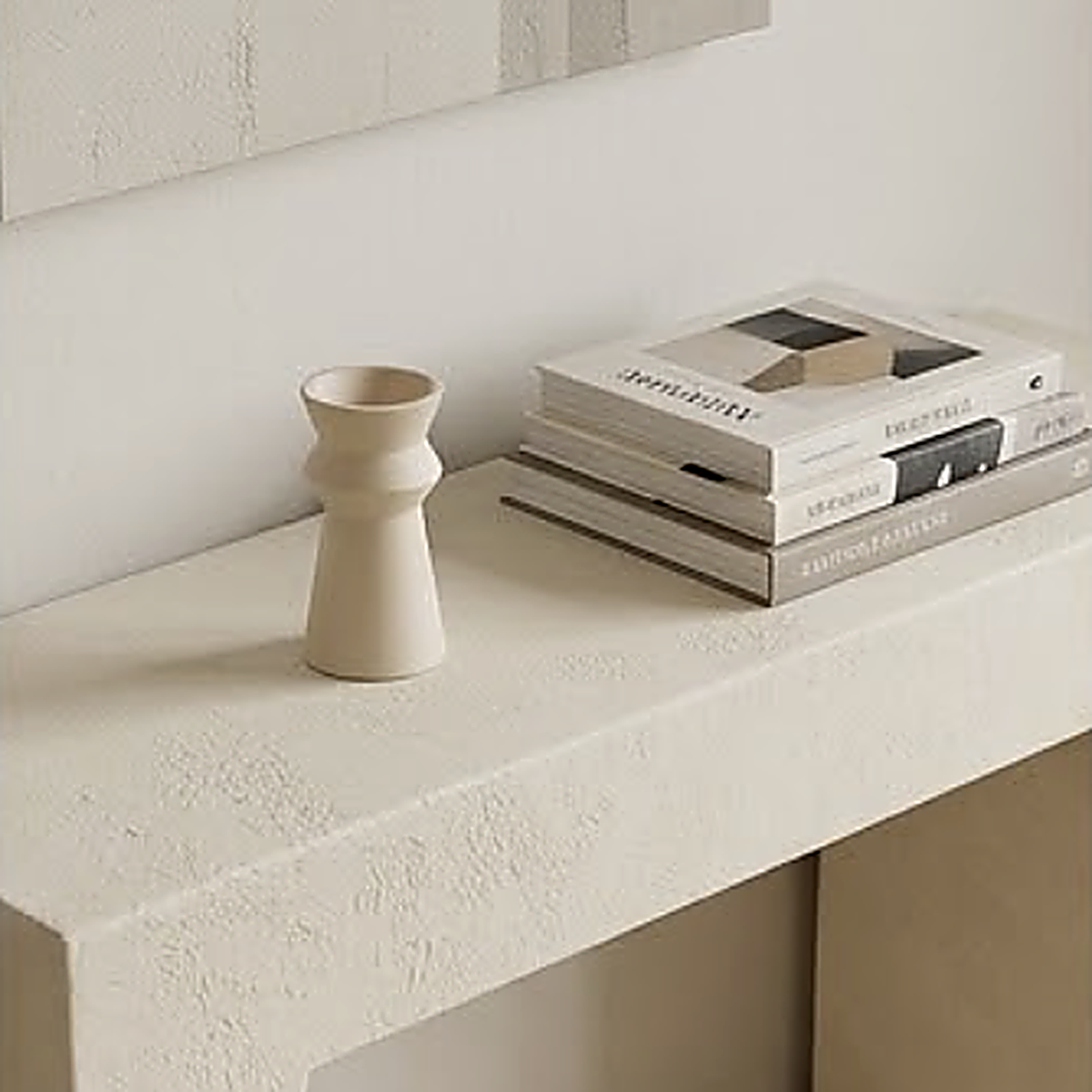 The candle holder unlit on a plaster console beside a stack of art books
