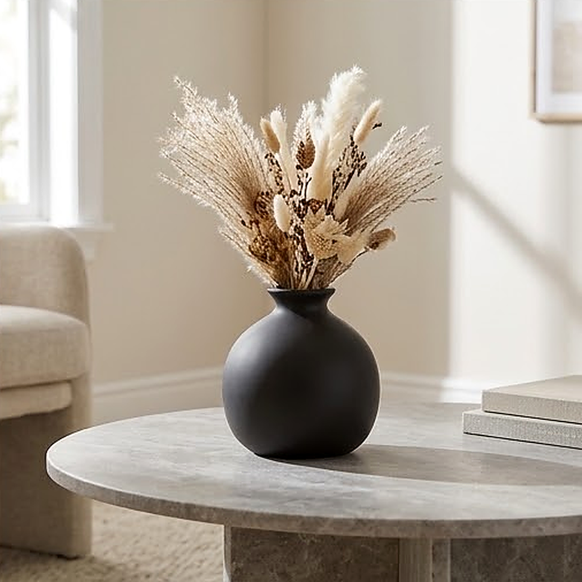 Matte black round ceramic vase with a flared rim, 10 cm, filled with dried pampas on a stone coffee table