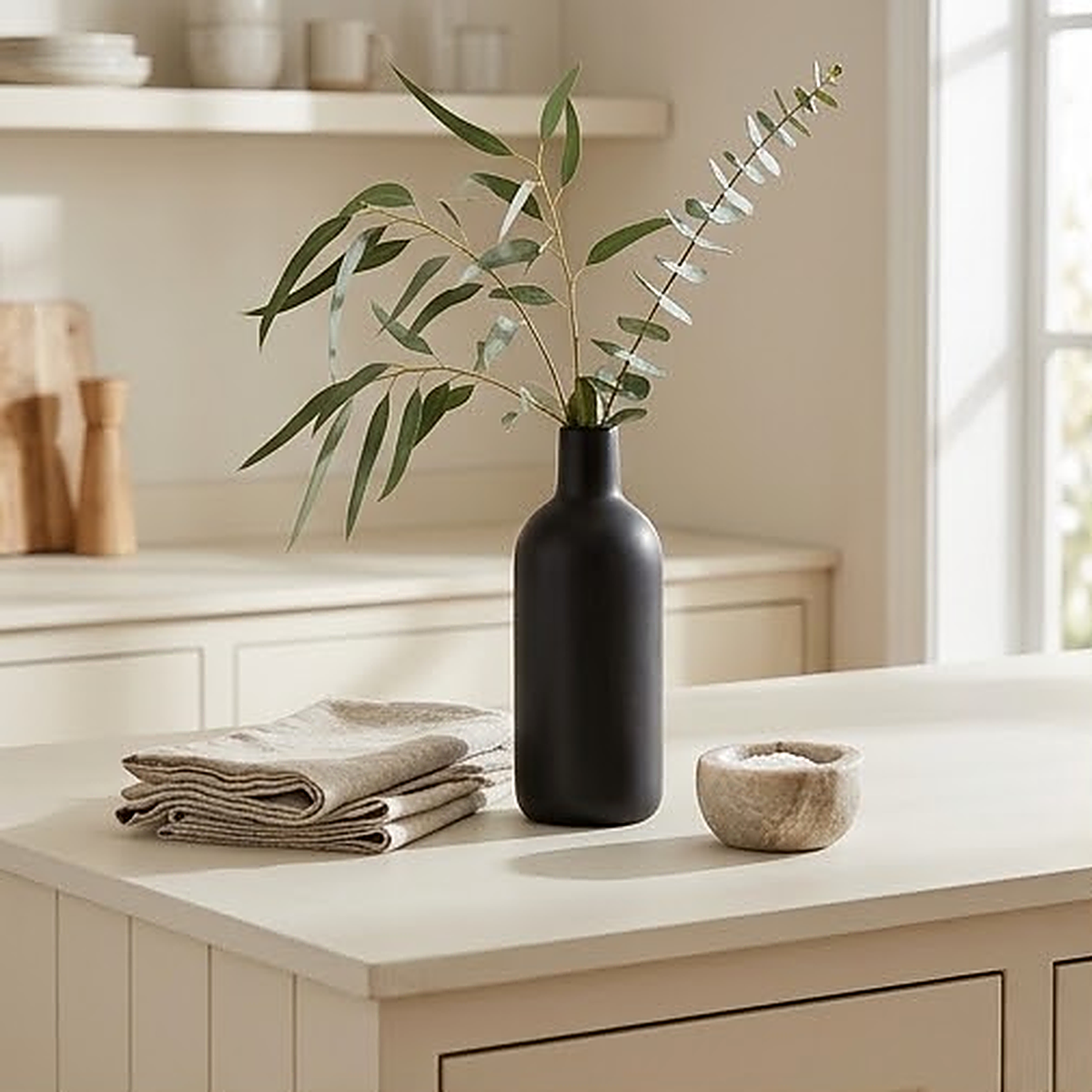 Matte black bottle shaped ceramic vase, 17.5 cm, holding eucalyptus on a pale kitchen counter